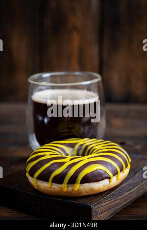Tasse schwarzer Kaffee mit Schokoladendonut auf hölzernem Hintergrund Stockfoto