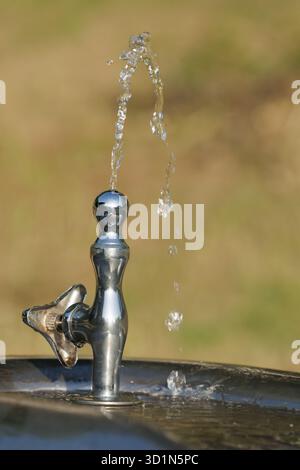 Elegante Bogenformen aus verchromtem Trinkbrunnen in einem Park im Freien. Sonnenlicht reflektiert das Metall des Brunnens und betont seine polierte Oberfläche. Stockfoto