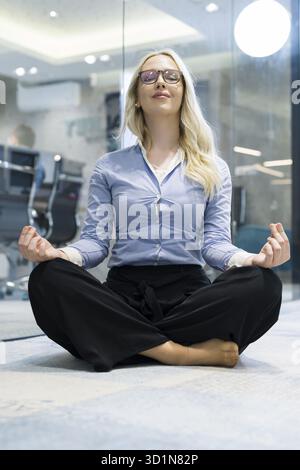 Jung betonte Hispanic Business-Frau beim Yoga in Bürogebäude, sitzen im Lotussitz mit Hände auf Knien. Konzept der langen Arbeitszeiten Stockfoto