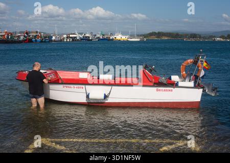 Weißes und rotes Schlauchboot mit seinem Besitzer an Land in O Grove Galicia Spanien Stockfoto
