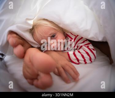 Verspieltes 4-jähriges Mädchen, das Spaß mit ihren Eltern im Bett hat Stockfoto