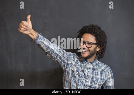Junger gutaussehender afro-amerikanischer Mann, der emotionale Possigna auf der Tafel macht, Hipster auf der Tafel Stockfoto