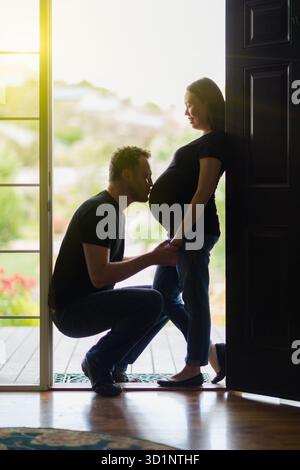 Ehemann küsst den Bauch einer schwangeren Frau in der Tür. Stockfoto