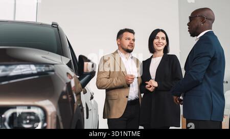 Verschiedene Gruppen diskutierten über den Kauf eines Fahrzeugs in einem modernen Händlerbetrieb und betonten ein stilvolles Fahrzeug und eine einladende Atmosphäre Stockfoto