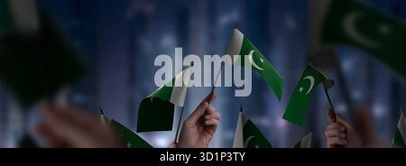 Pakistanische Flaggen in den Händen vor einem verschwommenen urbanen Hintergrund. Die Fotoillustration wurde ohne künstliche Intelligenz erstellt, nur mit Photoshop. Stockfoto