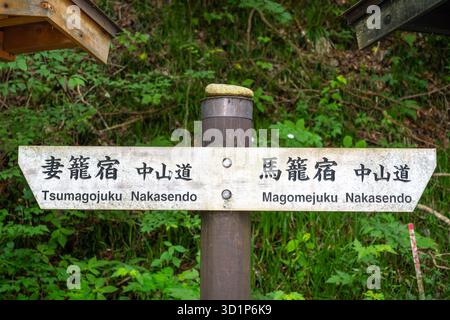 Ein zweisprachiger Wegweiser entlang des historischen Nakasendo Trail führt Reisende in Richtung Magomejuku und Tsumagojuku durch die üppige japanische Landschaft Stockfoto