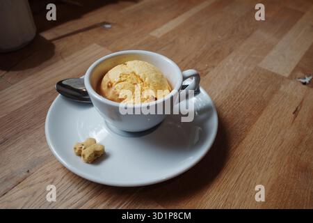 Ein einfaches, elegantes Dessert mit einem einzigen Messlöffel gelbem Eis oder Sorbet, serviert in einer weißen Kaffeetasse. Stockfoto