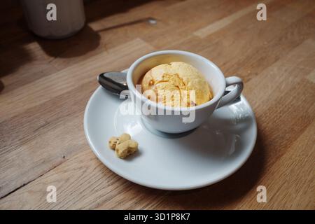 Ein einfaches, elegantes Dessert mit einem einzigen Messlöffel gelbem Eis oder Sorbet, serviert in einer weißen Kaffeetasse. Stockfoto