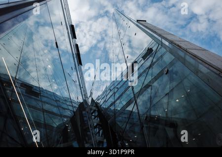 Ein dynamischer, flacher Blickwinkel (Wurmperspektive), der direkt in die Ecke eines modernen Wolkenkratzers aus Glas und Stahl blickt. Die stark reflektierende Fassade des Gebäudes Stockfoto