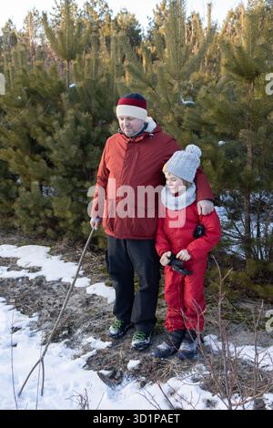 Dad und Sohn in warmen Kleidern schlendern im Winter durch einen verschneiten Park. Aktiver Lebensstil, Familienspaziergänge in der Natur. Stockfoto