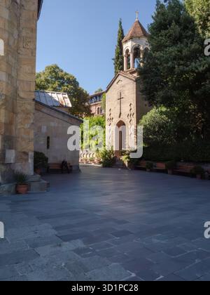 Die Kaschveti-Kirche St. Georg. Ruhiger Innenhof aus Stein, der zu einem kleinen historischen Kirchturm zwischen Bäumen und Schatten in Tiflis, Georgien, führt. Stockfoto