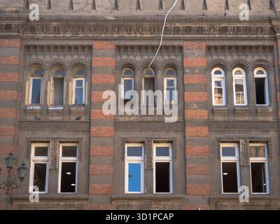 Alte Stadtfassade in Tiflis mit dekorativem Mauerwerk, roten Backsteinabschnitten, Bogenfenstern und historischen architektonischen Details. Stockfoto