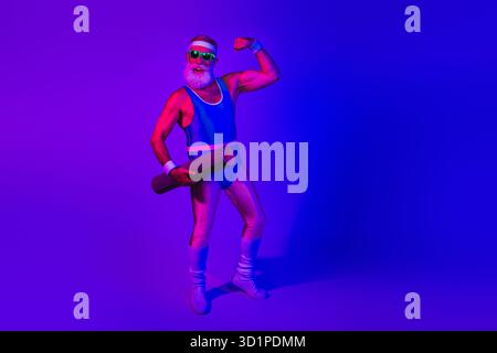 Retro-Fitness-Modell mit blauem Jumpsuit unter neonvioletter Beleuchtung, flexibler Arm und einer Matte in einem Studio-Porträt Stockfoto
