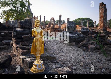 Die goldene Buddha-Statue steht vor einer Mauer. Die Statue ist von einem Steinhaufen umgeben Stockfoto