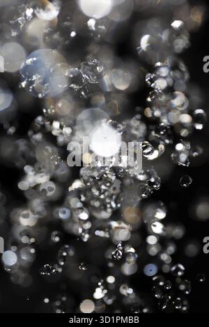 Wassertropfen fliegen in der Luft mit defokussierten Lichter auf Hintergrund Stockfoto