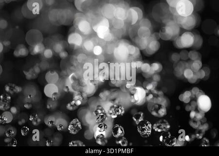 Wassertropfen fliegen in der Luft mit defokussierten Lichter auf Hintergrund Stockfoto
