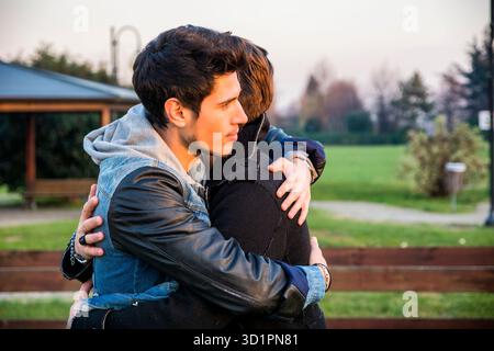 Glückliche männliche Freunde, die sich im Sonnenlicht umarmen Stockfoto