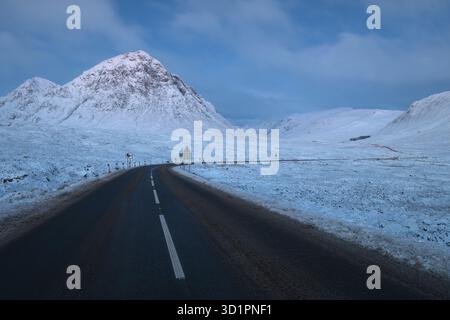 Eine nächtliche Winterlandschaft in den schottischen Highlands, Glencoe. Die schneebedeckte A82-Straße führt in Richtung des berühmten, schneebedeckten Berges Buachaille Etive Mor unter einem kalten blauen Himmel. Stockfoto