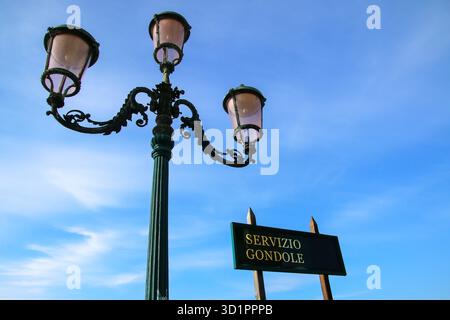 Schild mit Gondelservice und Straßenlaterne vor blauem Himmel in der Nähe des Markusplatzes in Venedig, Italien Stockfoto