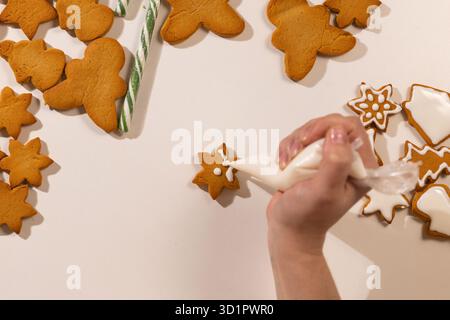 Eine Person dekoriert Lebkuchenkekse mit Zuckerguss und kreiert festliche Formen und Designs. Bei dieser fröhlichen Aktivität werden während der Weihnachtszeit traditionelle Kekse zubereitet. Stockfoto