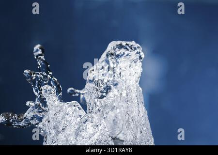 Wasserspritzer schweben in der Luft auf Blau. Schwebender Wassertropfen, vertikaler Schuss. Wassertropfen schweben in der Luft auf dem blauen Quadrat Stockfoto