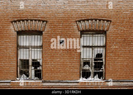 Zwei kaputte Fenster der alten Pflanze. Fenster mit Glasbruch an der alten roten Wand Stockfoto