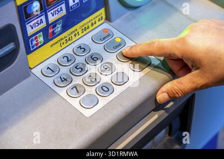 Denia, Alicante - Spanien - 22.12.2023: Nahaufnahme eines Fingers, der eine Taste auf der Tastatur des Geldautomaten drückt, mit Kartenlogos oben Stockfoto