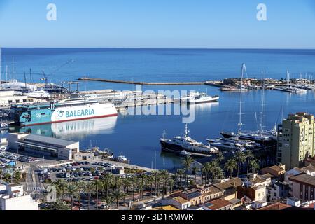 Denia, Alicante - Spanien - 12-22-2023: Panoramablick auf Denias Yachthafen mit Fähre, Yachten und palmengesäumter Promenade am Meer Stockfoto