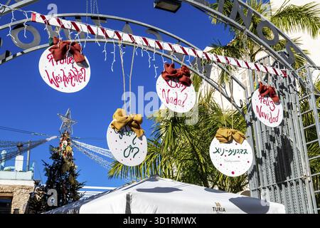 Denia, Alicante - Spanien - 22.12.2023: Hellblauer Himmel mit „Merry Christmas“-Schild in verschiedenen Sprachen an einem Markteingang Stockfoto