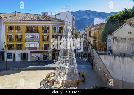 Denia, Alicante - Spanien - 12-22-2023: Hauptstraße in Denia, Spanien, mit festlichen Lichtern und einer Bergkulisse, bei der Einheimische spazieren gehen Stockfoto