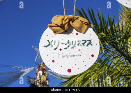 Denia, Alicante - Spanien - 22.12.2023: Hellblauer Himmel mit „Merry Christmas“-Schild in japanischem und orangefarbenem Band Stockfoto