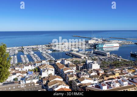 Denia, Alicante - Spanien - 12-22-2023: Panoramablick auf Denias Yachthafen mit Fähre, Yachten und palmengesäumter Promenade am Meer Stockfoto