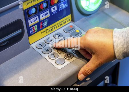 Denia, Alicante - Spanien - 22.12.2023: Nahaufnahme eines Fingers, der eine Taste auf der Tastatur des Geldautomaten drückt, mit Kartenlogos oben Stockfoto