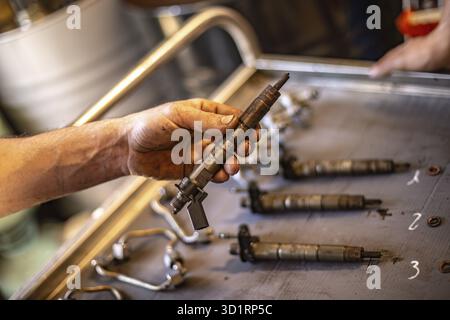 Nahaufnahme der schmutzigen Hände eines Mechanikers, die eine Einspritzdüse für Dieselmotoren halten, Schwerpunkt auf Reparaturarbeiten Stockfoto