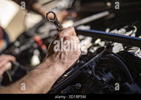 Nahaufnahme der schmutzigen Hände eines Mechanikers bei der Reparatur eines Automotors, wobei harte Arbeit gezeigt wird Stockfoto