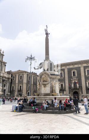 Catania, Sizilien - Italien - 15.04.2025: Menschen sitzen um den Elefantenbrunnen auf der Piazza del Duomo, Catania, mit barocken Gebäuden, Statuen und anderen Stockfoto