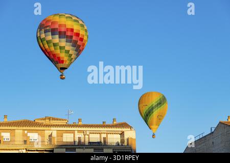 Guadix, Granada - Spanien - 24.01.2024: Zwei Heißluftballons schweben über Häusern mit roten Dächern, einer ist ein bunt karierter Ballon und der andere ist gelb Stockfoto