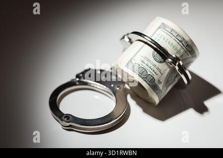 Handschellen auf Rolle von 100 Dollar-Scheinen unter Spotlight Stockfoto