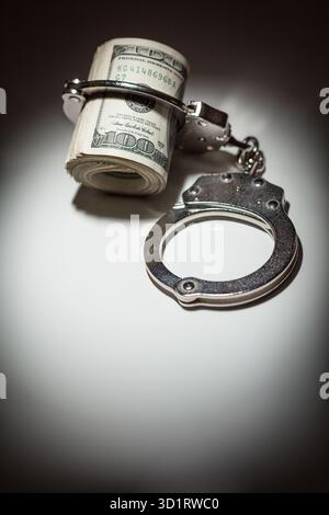 Handschellen auf Rolle von 100 Dollar-Scheinen unter Spotlight Stockfoto