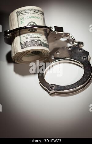 Handschellen auf Rolle von 100 Dollar-Scheinen unter Spotlight Stockfoto