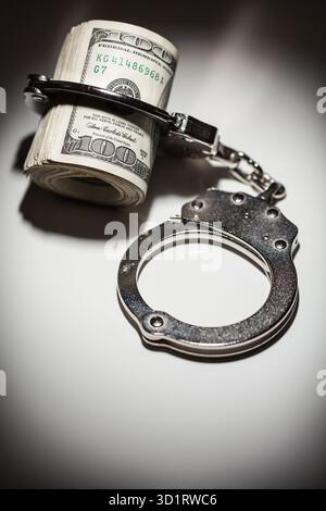 Handschellen auf Rolle von 100 Dollar-Scheinen unter Spotlight Stockfoto