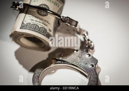 Handschellen auf Rolle von 100 Dollar-Scheinen unter Spotlight Stockfoto