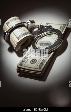 Handschellen auf Rolle von 100 Dollar-Scheinen unter Spotlight Stockfoto