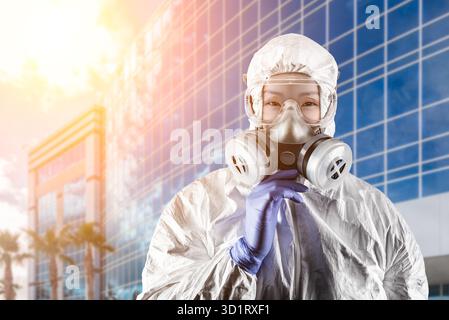 Chinesin mit Schutzanzug, Gasschutzmaske und Schutzbrille vor dem Stadtgebäude Stockfoto