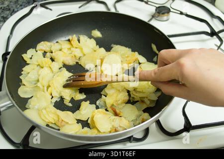 Mit einer Holzgabel die Kartoffeln in der Pfanne braten, um spanisches Omelett zuzubereiten Stockfoto