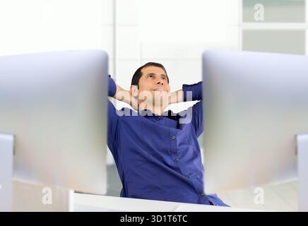 Entspannter Geschäftsmann im Büro auf seinen zwei Desktop-Bildschirmen Stockfoto