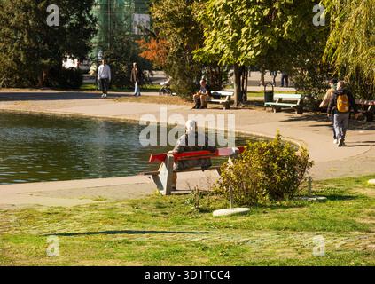 Mann sitzt auf einer Bank am Seeufer im Autumn Park Stockfoto