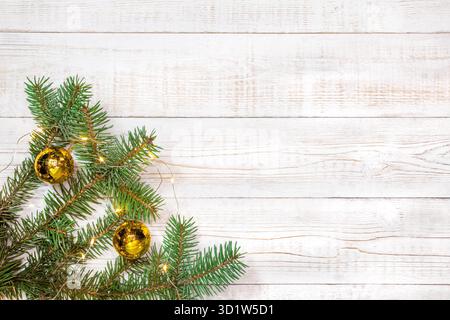 Weihnachtlicher Hintergrund - Tannenzweige mit goldenen Dekorationen und hellen Girlanden auf einem weißen Holztisch. Flaches Layout, Kompositionsrand in Draufsicht mit Cop Stockfoto