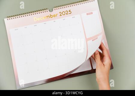Frau Hand dreht die Kalenderseite um. Die Kalenderseite für Dezember 2025 ist geöffnet und beginnt mit Neujahr 2026 Stockfoto