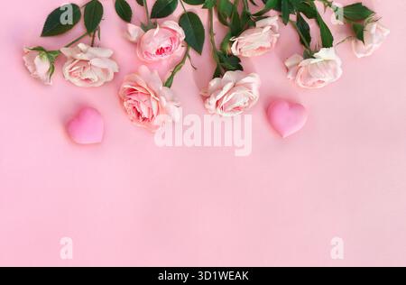 Rahmen von Blumen rosa Rosen mit Herzen auf einem rosa Papierhintergrund mit Platz für Text. Dekoration zum Valentinstag. Draufsicht, flach Stockfoto
